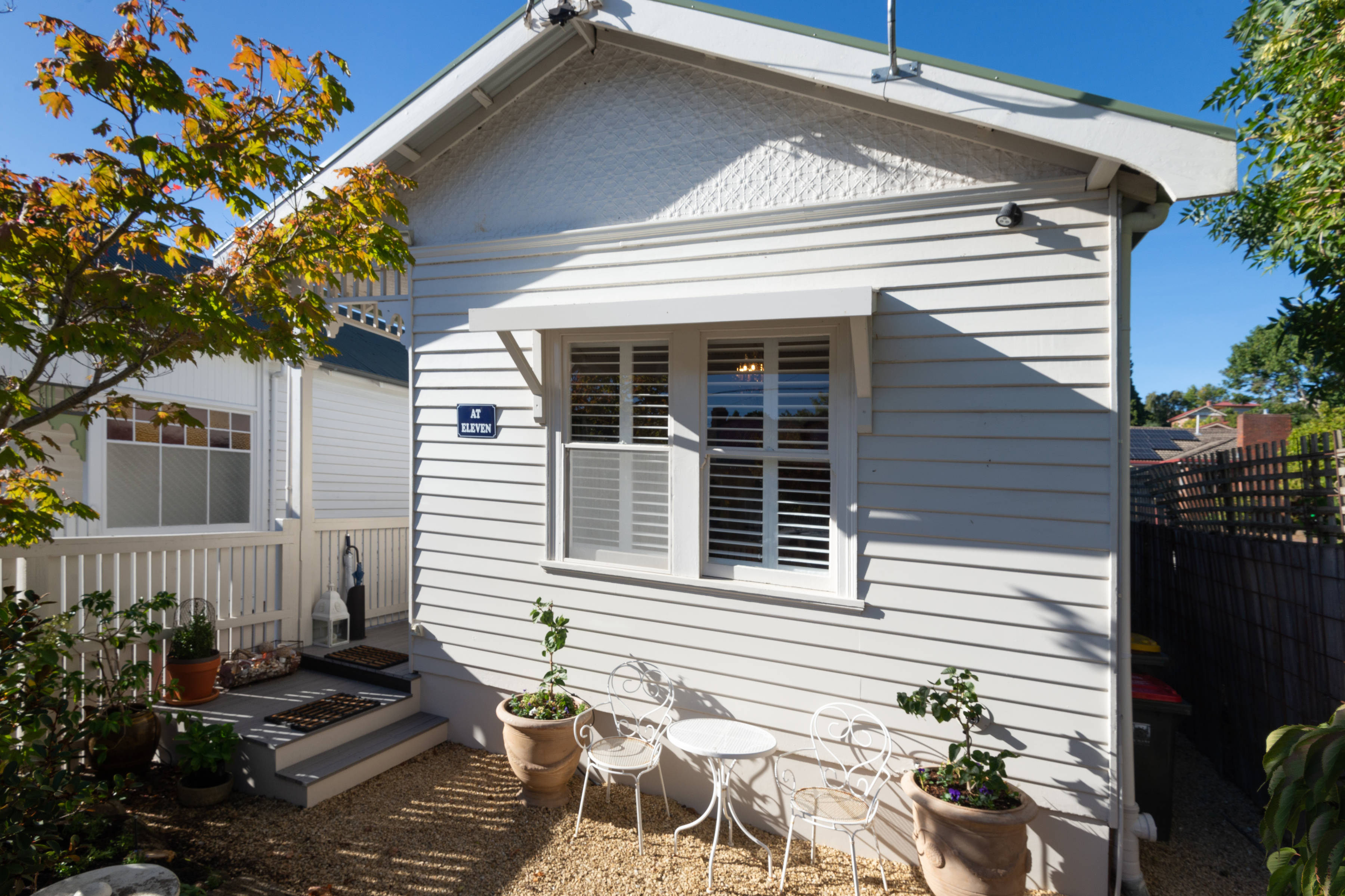 Front of cottage with porch and stairs, blue sky, front garden with flowers, small table and two chairs. Photo: Oliver Berlin.